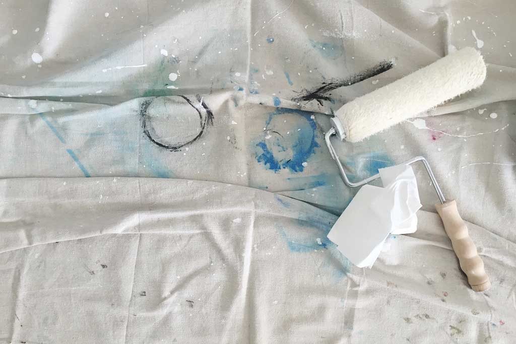 Painter roller laying on drop cloth splattered with paint