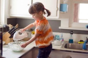 A young girls is mixing batter with an electric mixer in a kitchen