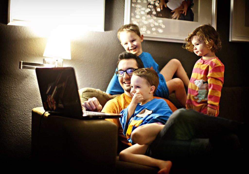Dad with three young children watching videos on a laptop.